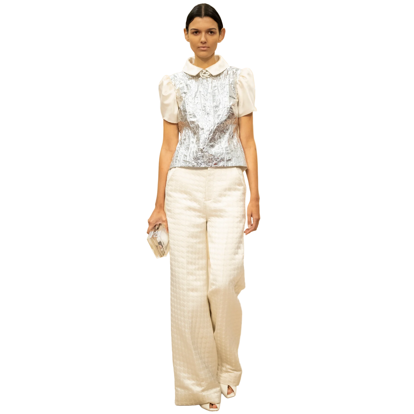 Model wearing a white outfit with a silver top in a fashion show setting.