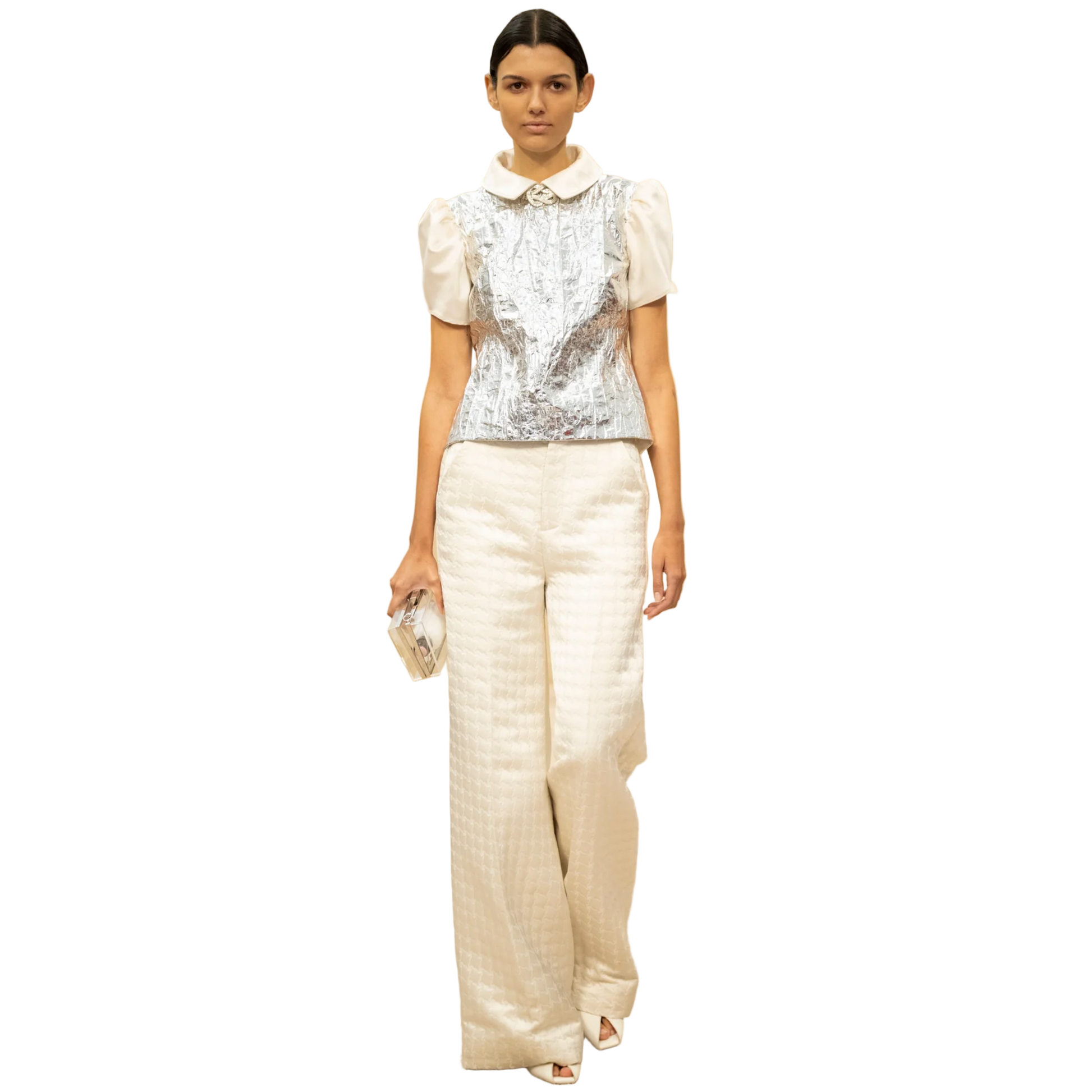 Model wearing a white outfit with a silver top in a fashion show setting.