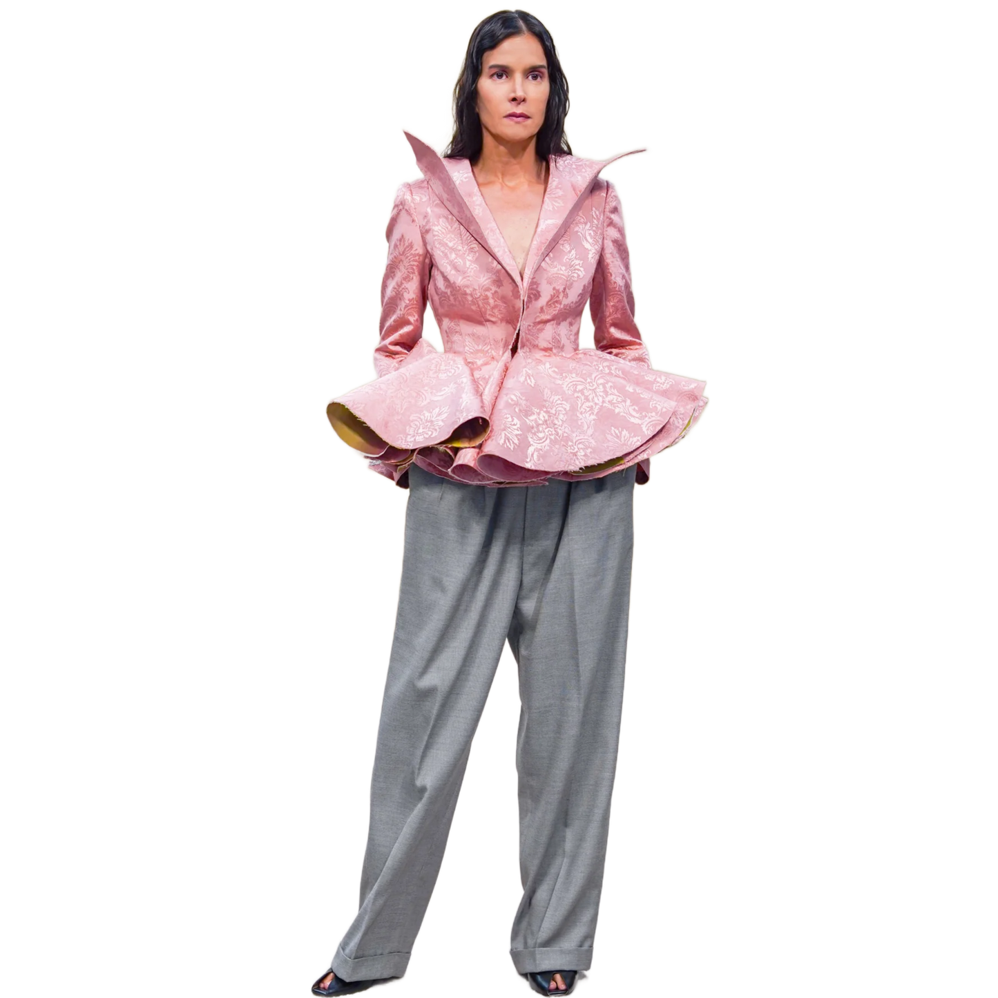Person wearing a pink jacket with ruffled details and gray pants on a white background