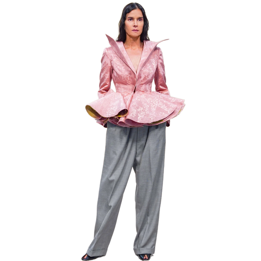 Person wearing a pink jacket with ruffled details and gray pants on a white background